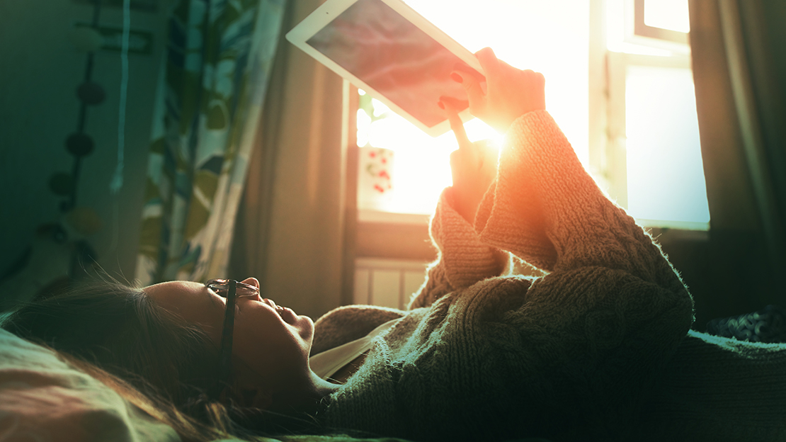 Kvinna ligger i sängen och använder surfplatta