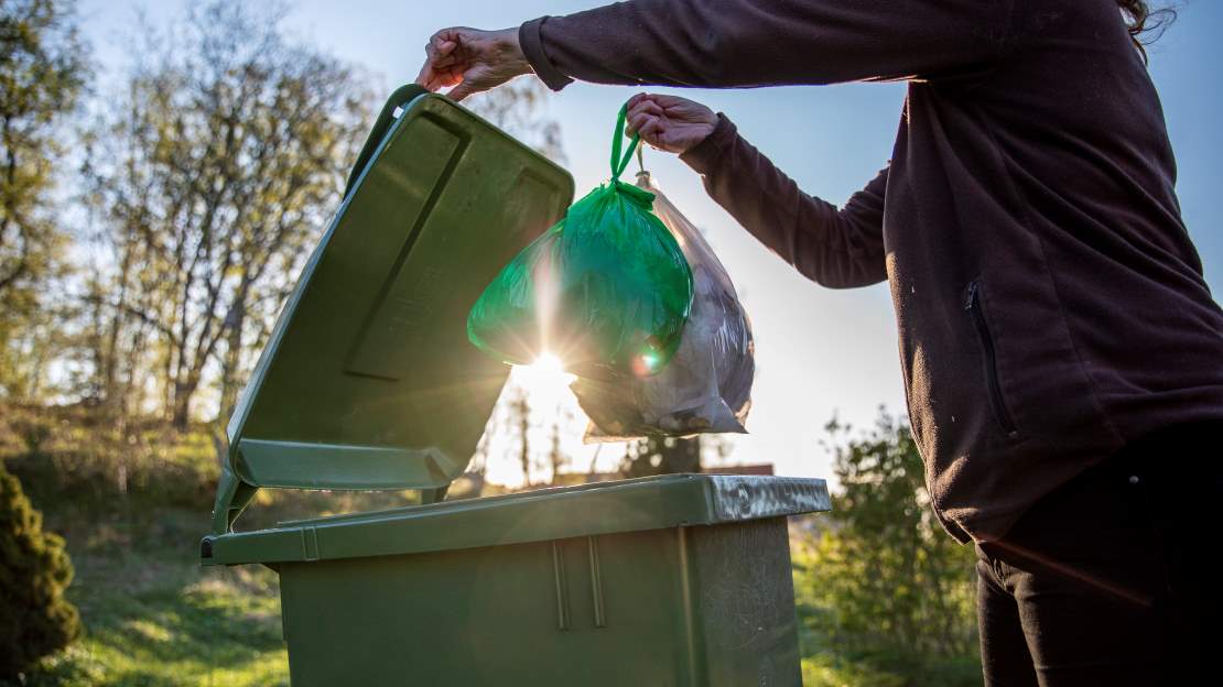 Grön påse slängs i avfallskärl
