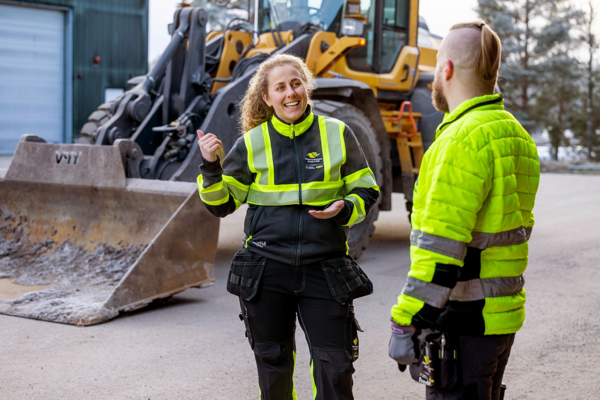 Två personer som pratar ute vid en grävmaskin